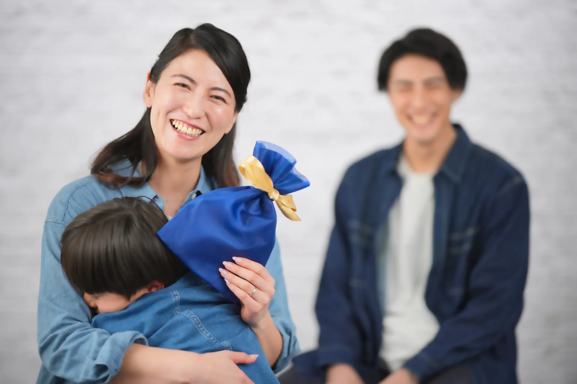 青い袋のプレゼントを持った母に抱きつく息子と笑う父